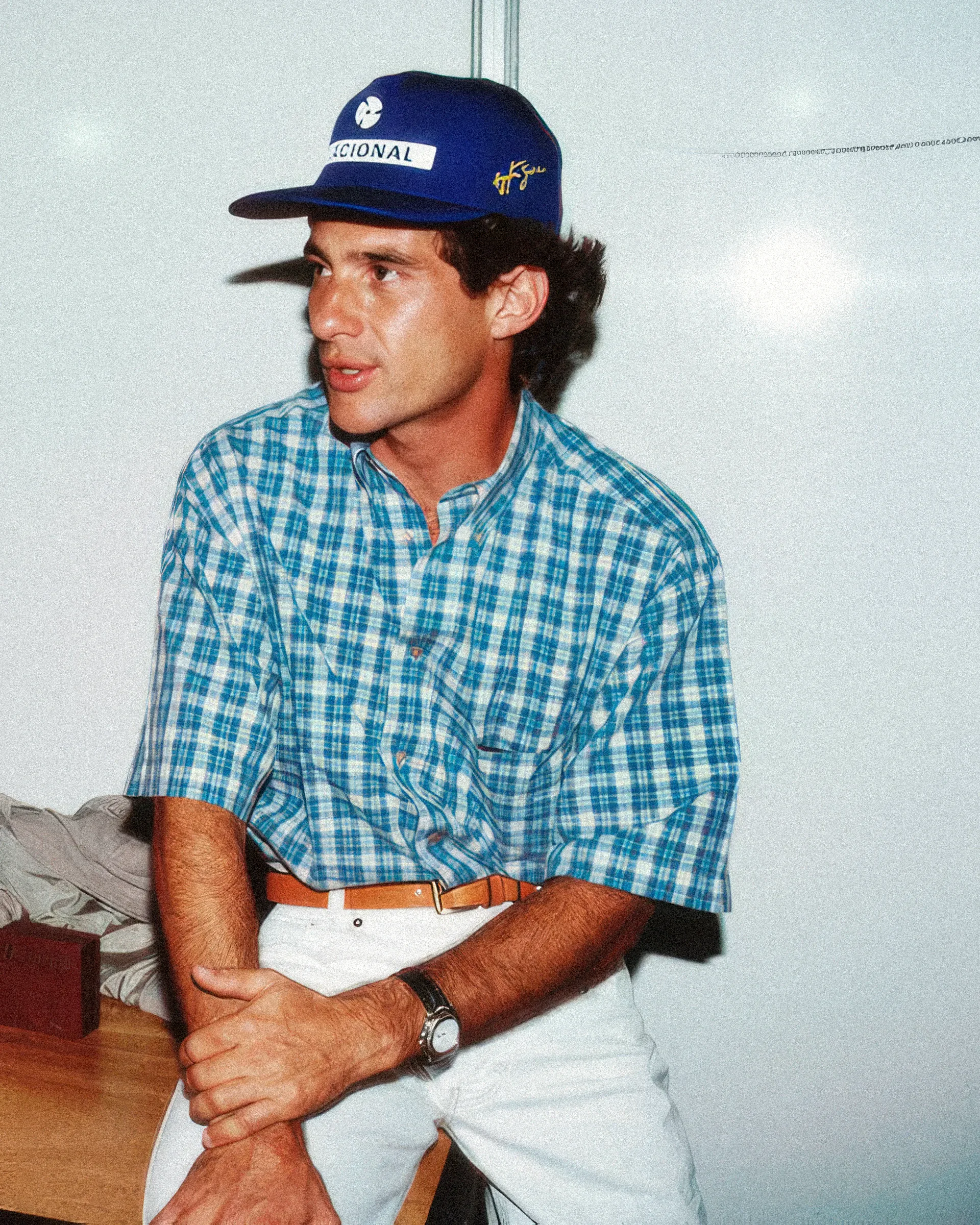Un uomo con un cappellino blu e una camicia a quadri, seduto.